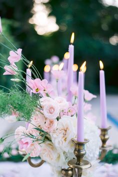 a vase filled with lots of flowers next to some purple and white candles on top of a table