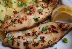 two fish fillets on a white plate with lemon wedges and green onion garnishes