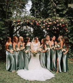 a group of women standing next to each other in front of some bushes and trees