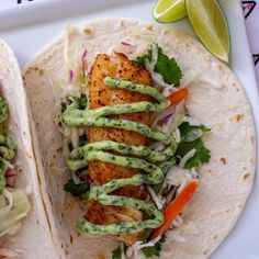 two fish tacos with guacamole and lime sauce on the side, sitting on a white plate