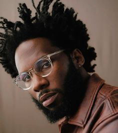 a close up of a person wearing glasses and a leather jacket with dreadlocks