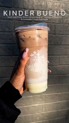 a woman holding up a cup of coffee in front of a brick wall with the words kinder bueno written on it