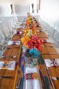 a long table is decorated with colorful flowers and napkins