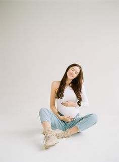 a pregnant woman sitting on the floor with her belly in her hands and smiling at the camera