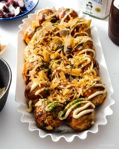 a white platter filled with meat covered in sauce and toppings next to other food items