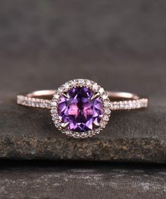 an oval shaped purple sapphire and diamond halo ring on top of a rock with diamonds around it