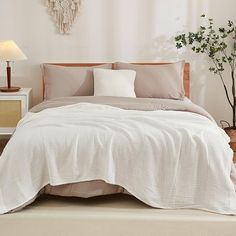 a bed with white sheets and pillows in a room next to a lamp on a table