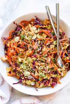 a white bowl filled with coleslaw slaw and two silver serving spoons