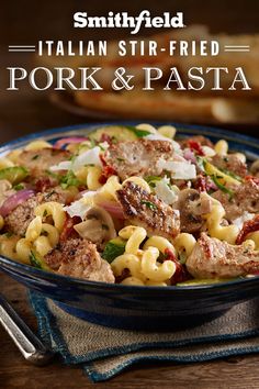 a blue bowl filled with pasta and meat on top of a table next to a fork