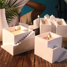 candles are lit in white boxes on a wooden table