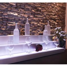 wine glasses and bottles are lined up on a shelf in front of a stone wall