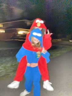 two people dressed in costumes walking down a street at night with their arms around each other