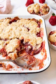 a close up of a plate of food with strawberry crumbles on it and two bowls of strawberries in the background