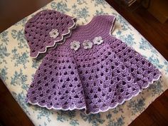 a purple crocheted dress sitting on top of a table next to a pillow