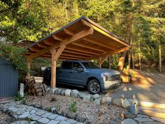 a pickup truck parked under a wooden carport in front of some trees and rocks