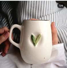 a person holding a white coffee mug with a green leaf on it