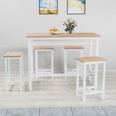 a white table with three stools in front of it and two pictures on the wall