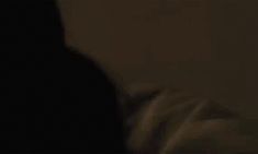 blurry image of person in dark room with white sheets on bed and headboard