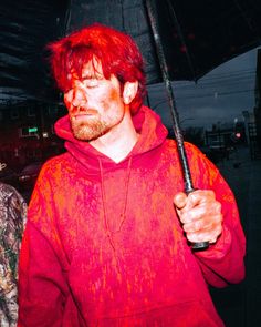 a man with red hair holding an umbrella in his hand while standing next to another man