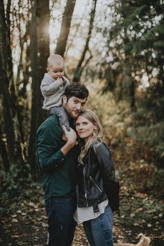 a man and woman holding a baby in the woods