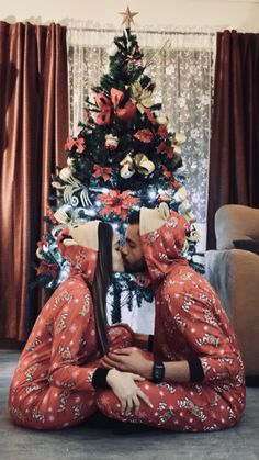 a man and woman sitting in front of a christmas tree with their heads touching each other