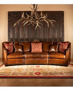 a brown leather couch sitting in front of a wooden wall with antlers on it