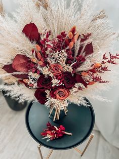 a bouquet of red flowers and white feathers sits on a blue table with gold legs