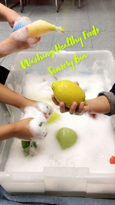 two children are washing their hands in a tub with soapy water and lemons