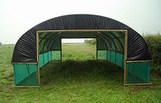 a green and black covered structure in the middle of a field