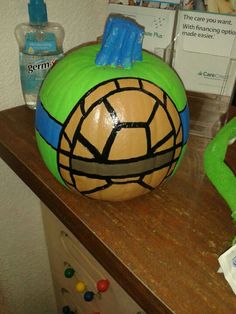 a green and yellow painted pumpkin sitting on top of a wooden table next to other items