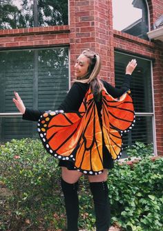 a woman wearing a butterfly costume standing in front of a brick building with her arms outstretched