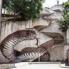 a large snake painted on the side of a wall next to stairs and trees in front of it