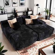 a living room filled with black couches and pillows on top of a wooden floor