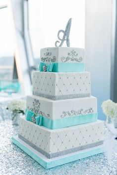 a three tiered white cake with blue ribbon and monogramming on it, sitting on a table