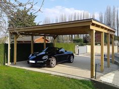 a black sports car is parked under a wooden carport in the driveway next to a fence