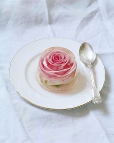 a plate with a pink rose on it and a spoon next to it, sitting on a white table cloth