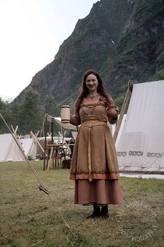 a woman dressed in medieval clothing holding a stick and bucket standing next to a tent