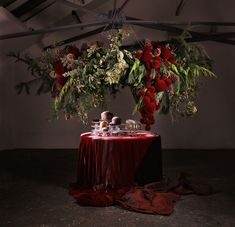 a table topped with lots of food and greenery next to a red cloth covered table