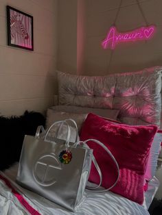 a white purse sitting on top of a bed next to a pink neon light sign