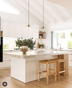 a large kitchen with white cabinets and wooden stools in the center island, surrounded by wood flooring