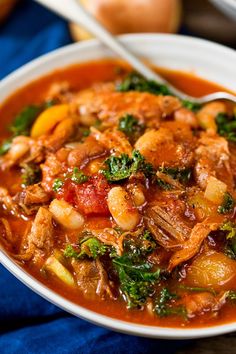 a white bowl filled with stew and vegetables on top of a blue cloth next to an onion