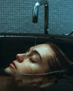 a woman laying down in a bathtub with water pouring from the faucet