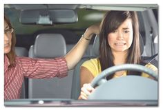 two women sitting in the driver's seat of a car and one is holding her head