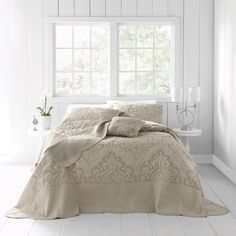 a bedroom with white walls and flooring has a bed covered in a beige comforter