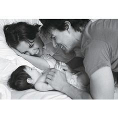 a black and white photo of a man, woman and baby laying on a bed