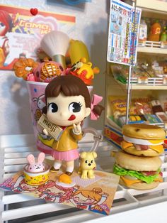 there is a toy girl that is standing next to hamburgers and other food items