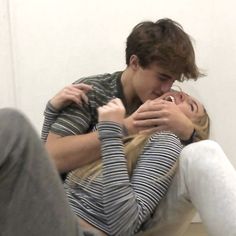 a man and woman cuddle together on the floor in front of a white wall