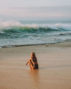 a woman sitting on top of a sandy beach next to the ocean with waves coming in