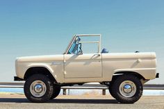 an old ford bronco pickup truck parked on the side of the road in front of a body of water