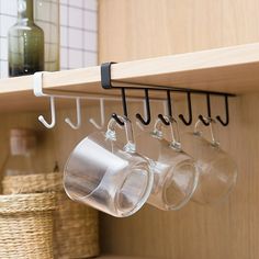 three wine glasses hanging from a wooden shelf in a kitchen with hooks and cups on it